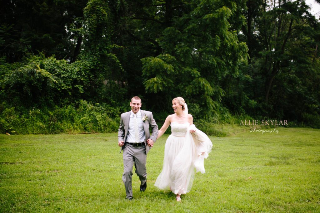 bride and groom sprint through a field in the rain