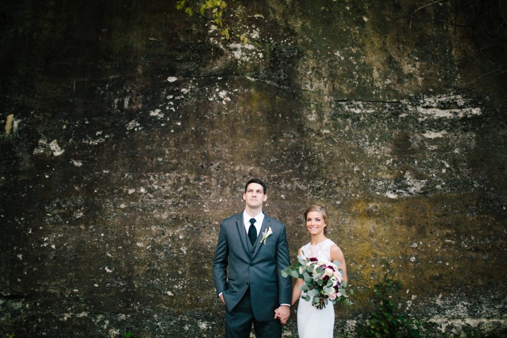 bride and groom pose in from of a stone wall at people light and theater in malvern