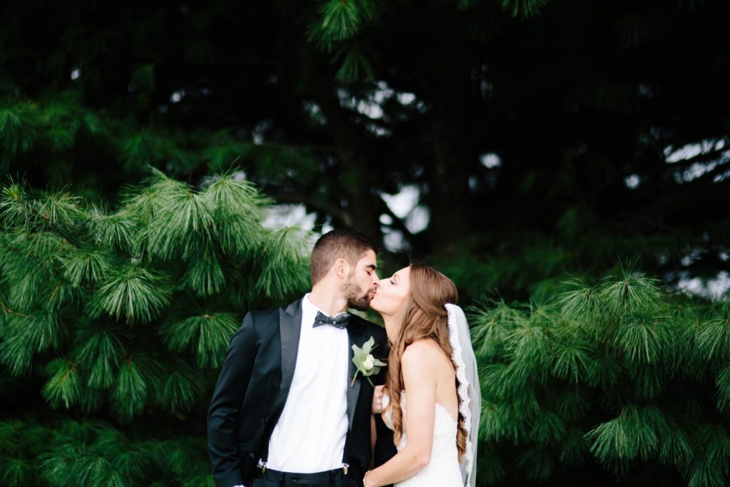 bride and groom share romantic kiss in front of pine tress at rose bank winery