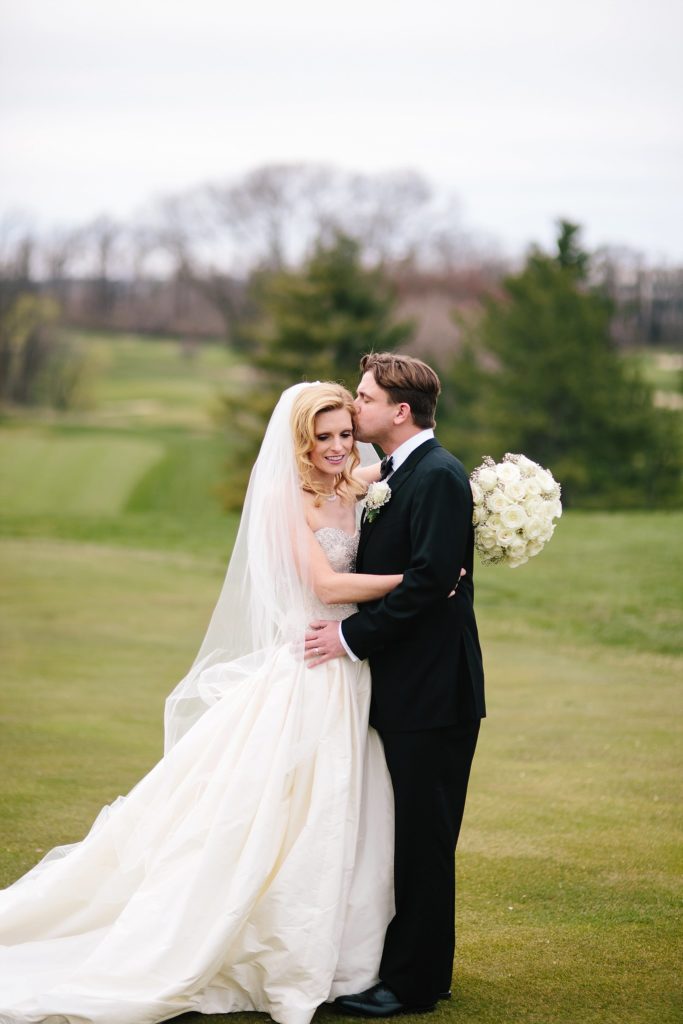 bride and groom embrace on the greens at Gulph Mills Golf Club outside of Philadelphia for their spring wedding