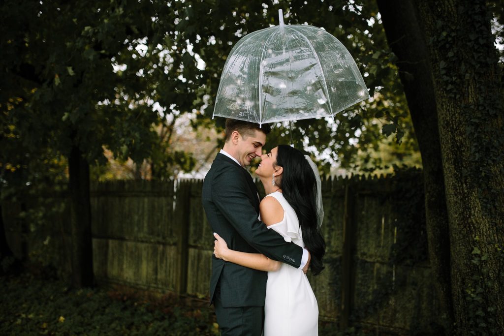 bride and groom embrace under an umbrella before their wedding at terrain gardens in devon pa
