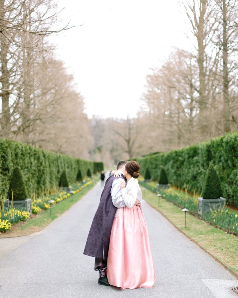 korean bride and groom pose in the  longwood gardens during their engagement session wearing their traditional hanboks