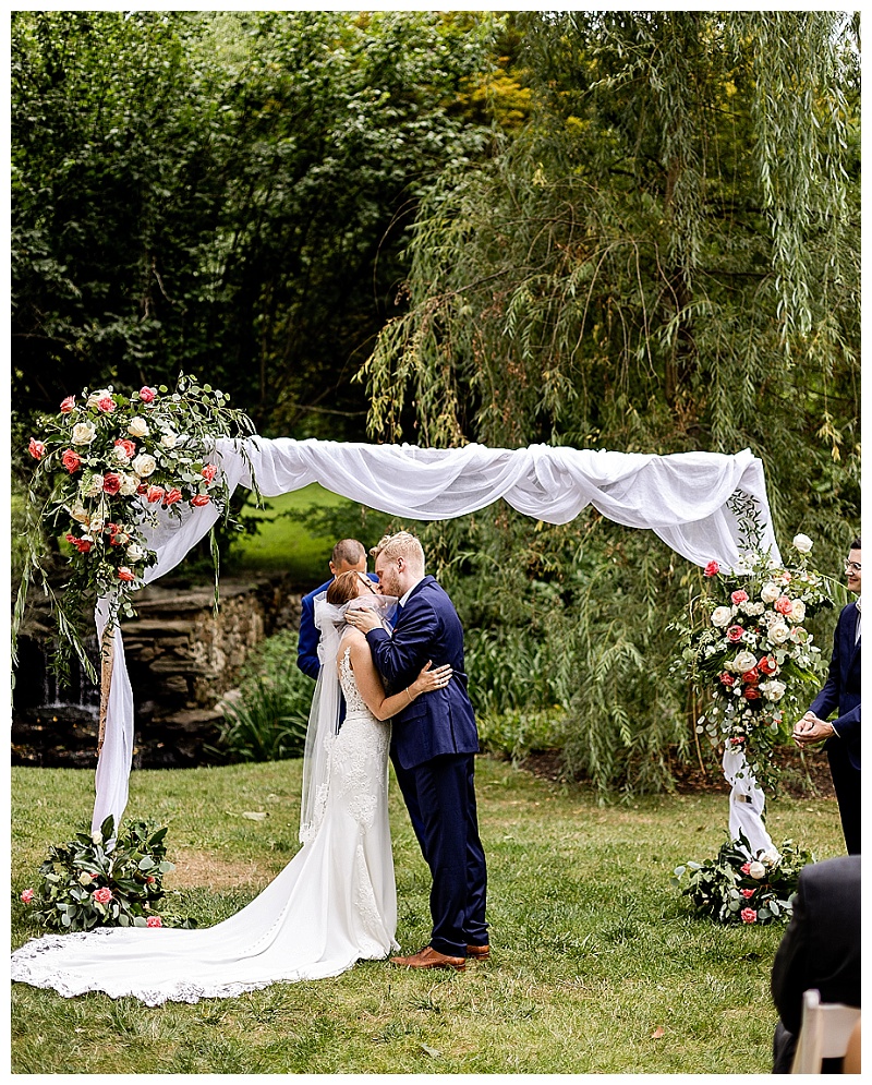 bride and groom are married under an arch of flowers at their outdoor summer wedding at Appleford Estate in Villanova PA