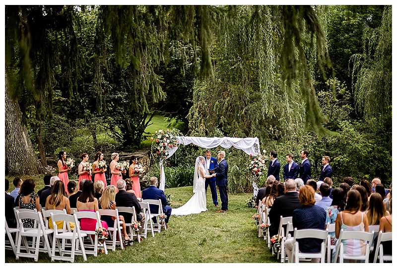 bride and groom are married under an arch of flowers at their outdoor summer wedding at Appleford Estate in Villanova PA